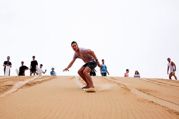 Tourists enjoying sandboarding on the Timlalin Dunes near Agadir, Morocco.